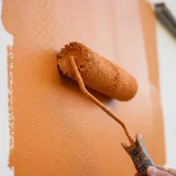 Gros plan sur l'application d'une peinture de couleur orange sur la façade d'une maison rénovée